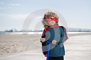 Child on scooter in park. Kids learn to skate roller board. Power kids, super hero child in a superhero raincoat.