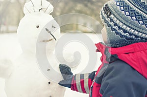 A child sculpts a snowman in the winter on the street, a boy in a red overall