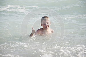 child on sea with waves. Hand with thumb up.