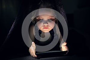 Child secretly using phone in bed under the blanket in dark room