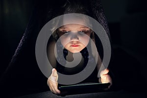 Child secretly using phone in bed under the blanket in dark room photo