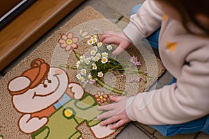 child setting a small daisy bunch on a cartooncharacter door mat