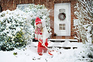 Child shoveling snow. Little girl with spade clearing driveway after winter snowstorm. Kids clear path to house door after