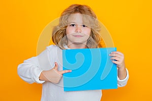 Child showing index finger on sheet of paper, isolated on yellow background. Portrait of a kid holding a blank placard