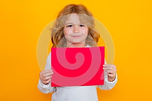 Child showing red sheet of paper, isolated on yellow background. Portrait of a kid holding a blank placard, poster