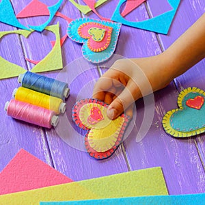 Child shows a felt heart ornament. Kid made a felt heart for Valentines Day. Bright felt hearts, thread set, felt sheets and piece