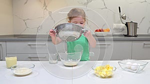 Child sieving flour into a bowl. Kid is playing with a flour.