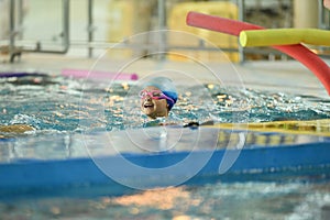 A child in a silicone cap and glasses learns to swim in the pool