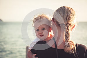 Child with a sincere look hugging his mother sitting on her hands and looking at camera