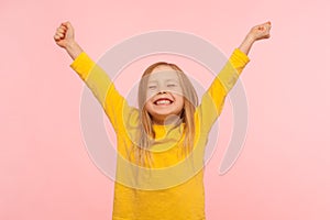 Child sincerely rejoicing success. Cute energetic enthusiastic little girl raising arms in excitement