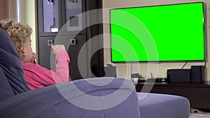 Child sit in front of a tv and watch a children show on. Green chroma key screen