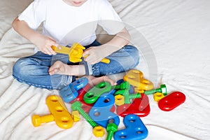 The child sits on the bed and plays the constructor. Hands tighten the bolt and nut. Children`s creativity and learning. Home