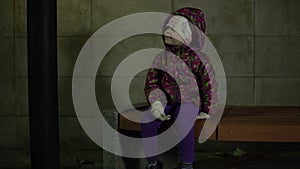 The child sits on a bench under the light of a lantern at night in the park.