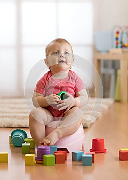 Child sits on chamber pot, toilet, playing with toys