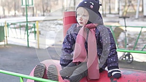 A child sits on a cold toy locomotive on the street in winter