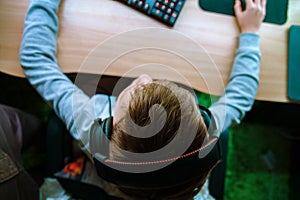 The child sits at the computer and plays computer games in the headphones. Top view of the hand holding the mouse and keyboard.