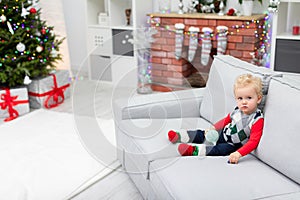 A child sits on the couch and waits for presents from under the Christmas tree