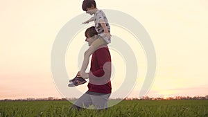 Child sits on daddy's shoulders. Happy family dad with son play together in the field. Father and child spend time