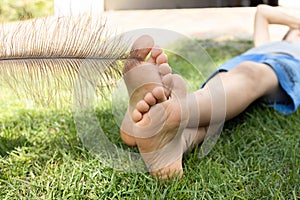 child sits on the lawn in the summer his bare feet are tickled with a large ostrich feather