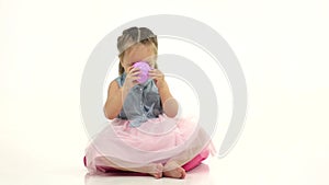 Child sits on a pillow and drinks tea. White background. Slow motion