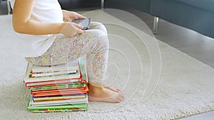 Child sits on a stack of children's fairy-tale books and watches cartoons on her smartphone