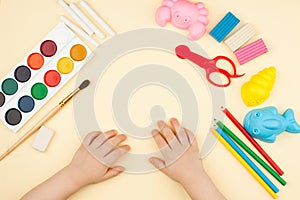The child sits at the table with objects for creativity, drawing and hobbies, the top view.