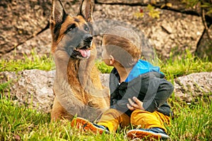 Child sits turning with a German shepherd in nature