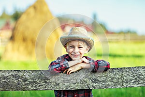 Little boy sits on wooden fence against picturesque haystack