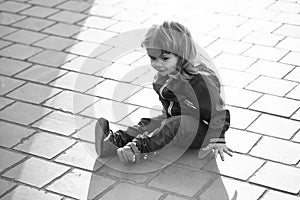 Child is sitting on the asphalt. Little boy sits on pavement