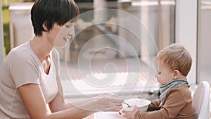 Child sitting in a baby chair and eating food with mother