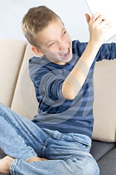 Child sitting on couch and using tablet computer. Teen boy annoyed and frustrated shouting with anger while playing computer games