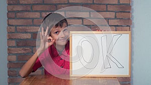 Child sitting at the desk holding flipchart with lettering ok on