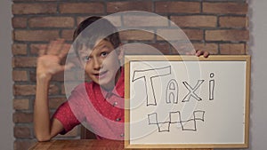 Child sitting at the desk holding flipchart with lettering taxi on the background red brick wall