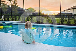 Child sitting on the edge of a swimming pool on a warm summer day