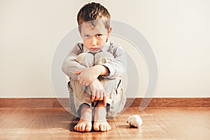 Child sitting on the floor barefoot with sad face for not being able to put on his clothes