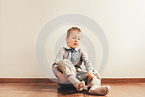 Child sitting on the floor putting on his socks with an expression of effort, concept of autonomy