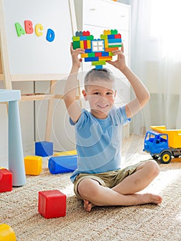 Child sitting on the floor in the room playing. Bright building blocks in the shape of a heart in the hands of children