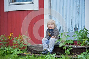 Child sitting in front of a red house in Norway, summer