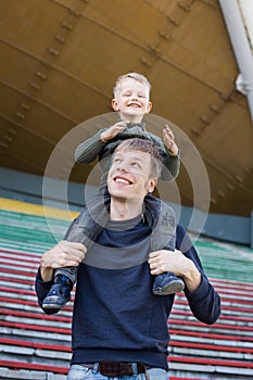 The child is sitting on his dad's shoulders and looks happy