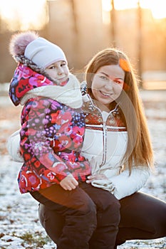 Child sitting with mother on a walk in park, the sun's rays of sunset