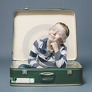 Child sitting in an old suitcase smiles imagining a journey