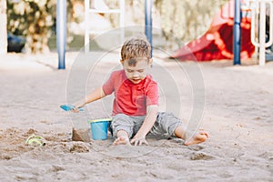 Child sitting in sandbox playing with beach toys. Boy building sandcastle or sand pie from sand. Kid have fun on playground.