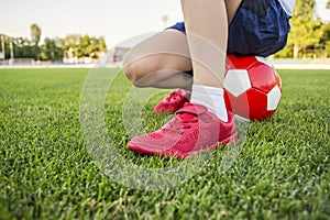 A child is sitting on a soccer ball on the grass of stadium`s field. Training and sports for children concept