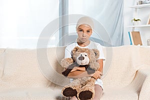 Child sitting on sofa and holding teddy bear