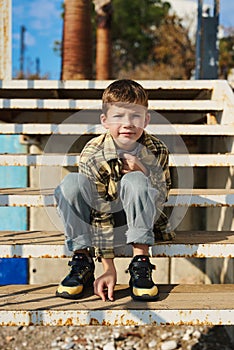 Child sitting on the steps. Portrait of handsome kid boy wearing casual sitting on the stairs on the street. Stylish boy