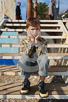 Child sitting on the steps. Portrait of handsome kid boy wearing casual sitting on the stairs on the street. Stylish boy