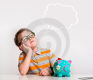 Child sitting at the table with money and piggy bank and dreaming. Happy boy with euro coins. Kid dreaming about future