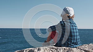 Child sitting on the top of the mountain and watching sea waves