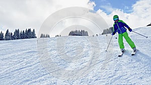 Child ski downhill to camera on skiing track at alpine resort