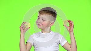 Child with slices of lemon licks them and shows grimaces. Green screen. Slow motion